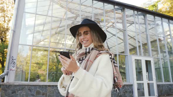 Young Woman in the Hat Chatting with Friend Using Smartphone