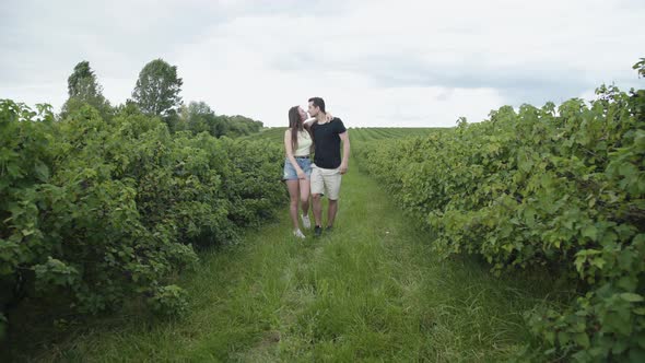 Happy Girlfriend Leads Her Man in Embraces Among Currant Plantation