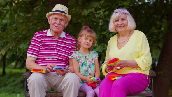 Smiling Senior Grandmother Grandfather with Granddaughter Playing Squeezing Antistress Toy Game