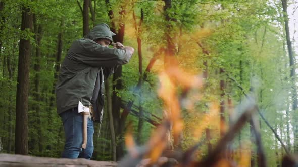 Slow Motion Of Casual Strong Man Works with Ax and Firewood Near Warm Bonfire in Camp in Wild