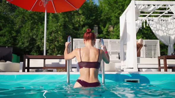 Attractive Woman in Swimsuit with Beautiful Figure Climbs Out From the Pool