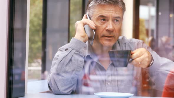 Businessman talking on mobile phone while having cup of coffee