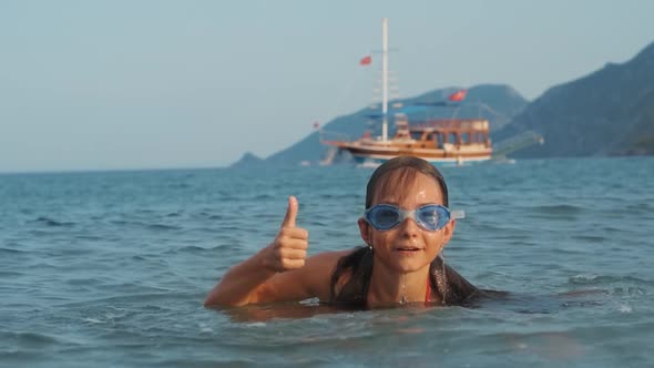 Girl Emerging From Sea and Showing Thumb. Joyful Kid Bathing Into Sea