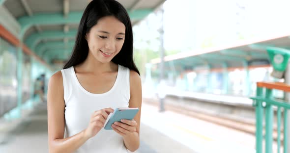 Woman using mobile phone and walking in the light rail station 