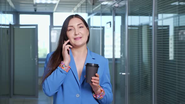 Serious Businesswoman Talks on Smartphone Holding Coffee Cup