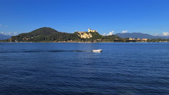 Small motorboat navigating in calm lake waters of Maggiore lake in Italy with Angera castle in backg