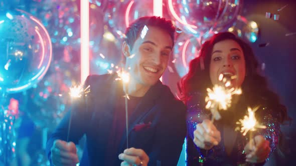 Happy Man and Woman Holding Sparkles in Club. Couple Dancing with Bengal Lights