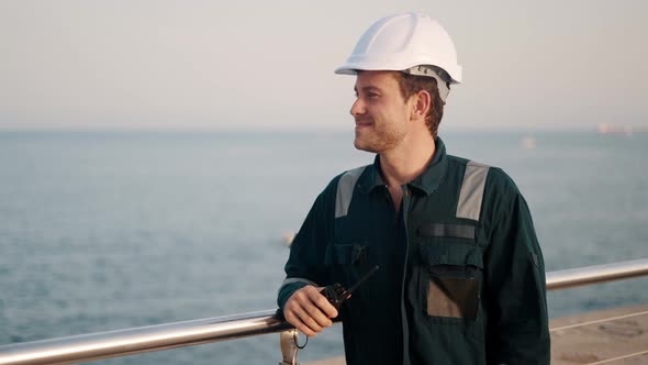 Happy Dock Worker with Walkietalkie in Hand Standing in Port Terminal Enjoying Sea View