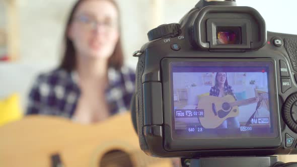 Young Woman Blogger Sitting on the Couch Playing Guitar Shot Through the Camera Screen