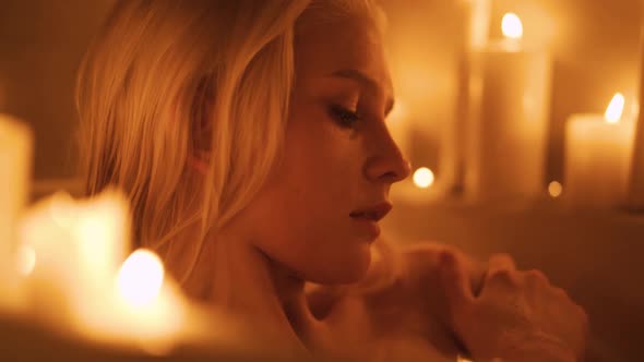 Young Girl Relaxes in the Bath By Candlelight and Blows Off the Foam