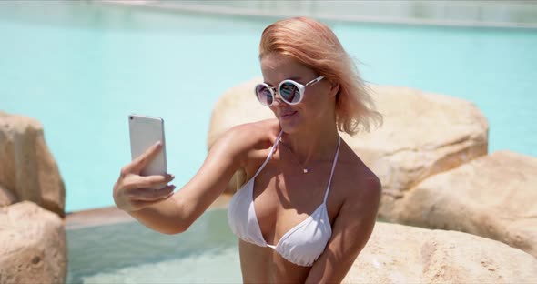 Smiling Woman in Swimwear Taking Selfie on Smartphone Showing Two Fingers