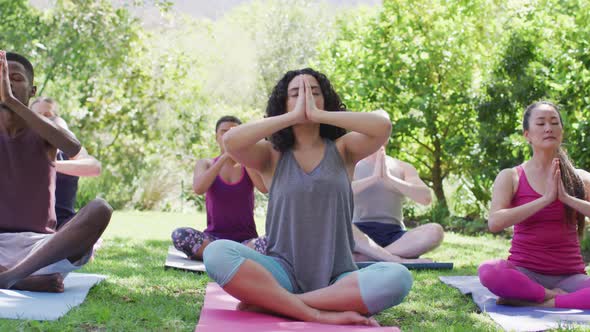 Group of diverse young people meditating and practicing yoga together at the park