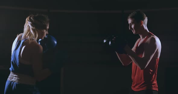 Beautiful Brunette Boxer Working Out Blows To the Paws with a Trainer in a Dark Room