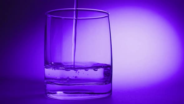 Studio Shoot of Water Pouring Into Transparent Glass on Blue Background