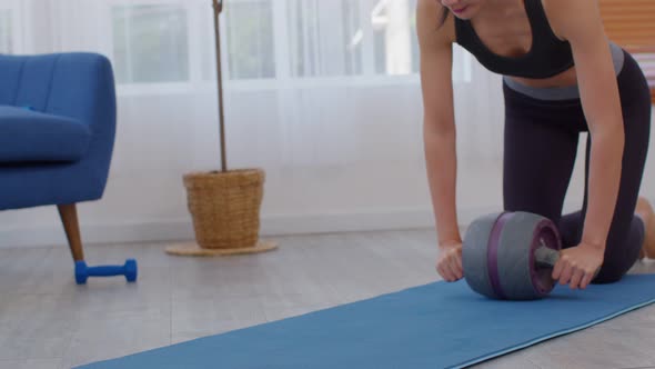 Athlete Asian young woman exercise with ab roller on exercise mat at home