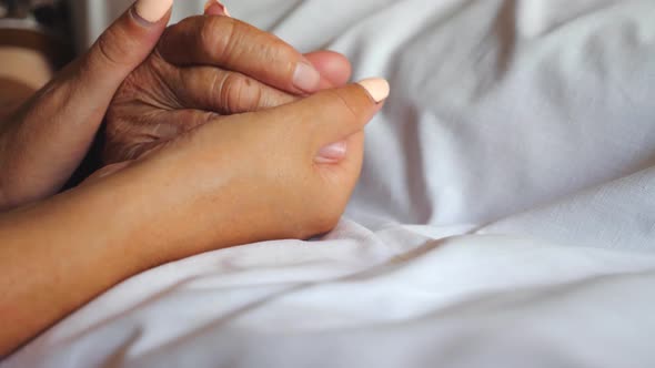 Unrecognizable Woman Holding Hand of Her Old Mother Lying in Bed Showing Care or Love. Daughter