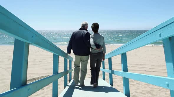 Couple walking on walkway and on beach towards the sea