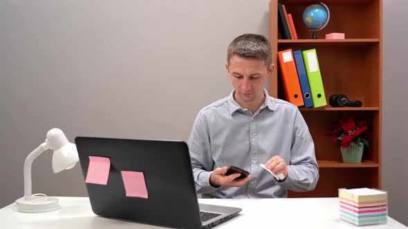 Young Guy Office Worker Manager Disinfects a Smartphone During a Pandemic