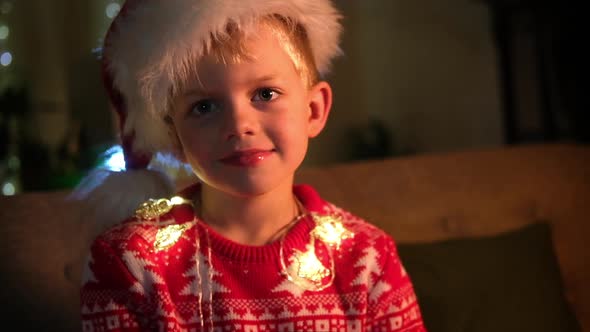 Portrait Smiling Laughing Boy in Santa Hat and Christmas Costume Sitting at Home