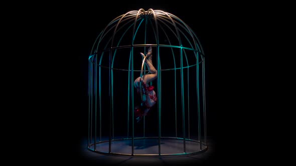 Actress in a Red Costume on a Gymnastic Hoop Performs Tricks in a Cage . Black Background. Slow