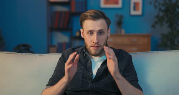 A Shocked Man is Sitting on a Couch in the Living Room in Front of