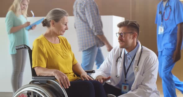 Doctor Talking to Senior Woman in Wheelchair at Clinic Waiting Room