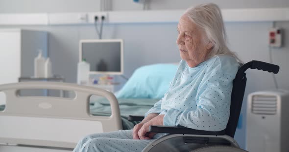 Senior Sad Woman Sitting in Wheelchair in Hospital Ward