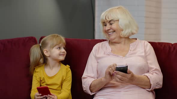 Senior Grandmother with Child Girl Granddaughter Using Digital Mobile Phone, Playing Games at Home