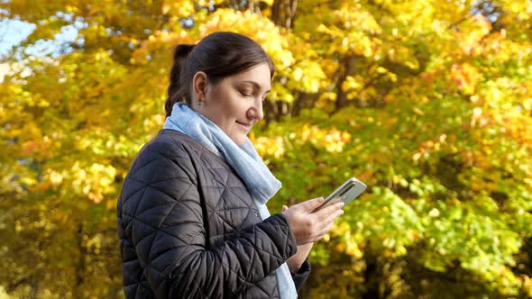 Young Woman with Phone on Background of Yellow Trees