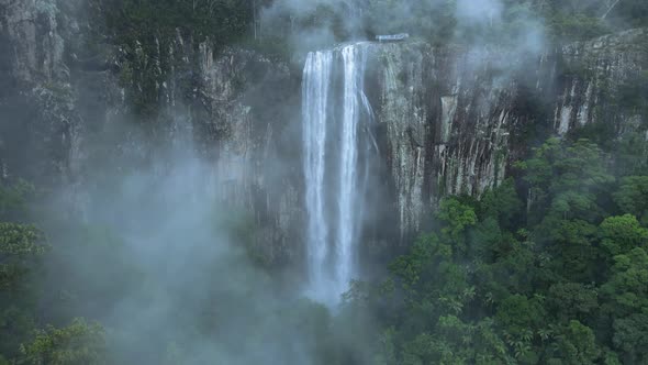 Cinematic view looking through rising mist revealing a majestic waterfall spilling over a lush rainf