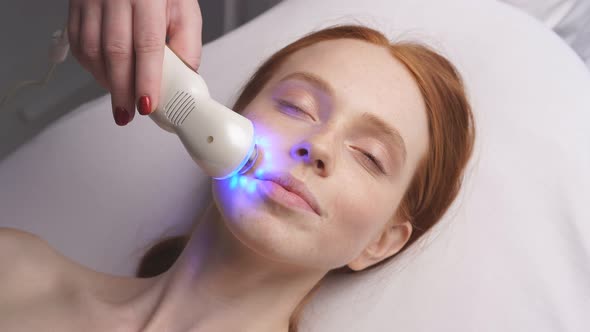 Cosmetologist Moves the Manipulator with a Cooling Blue Light Over the Skin of the Face. Hardware
