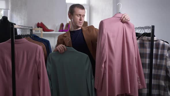 Portrait of Unsure Elegant Gay Man Choosing Blazer in Shop Indoors Thinking