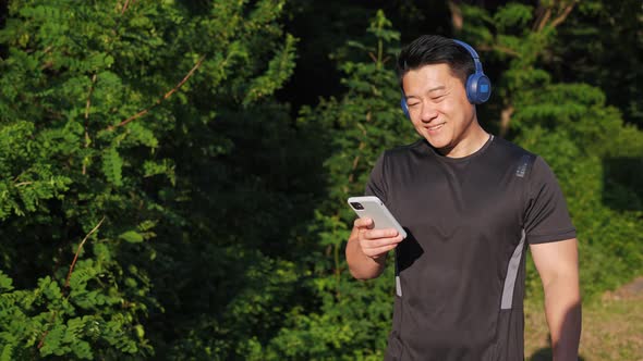 Korean Jogger Wearing Wireless Headphones Holding Mobile Phone Listening Music