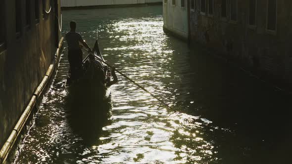 Silhouette of Gondolier Steering Boat in Venice Street, Sun Reflection in Water