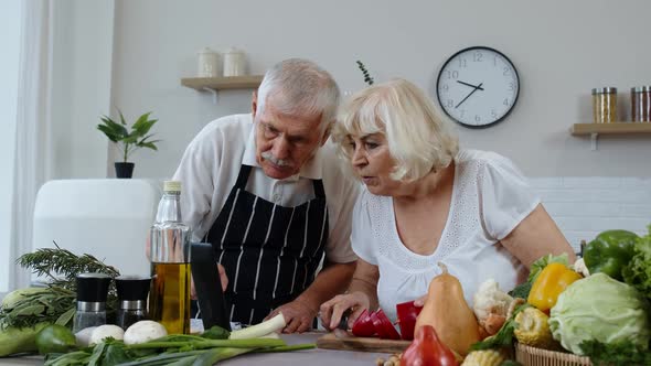 Vegan Senior Couple Cooking Salad with Raw Vegetables. Looking on Digital Tablet for Online Recipe