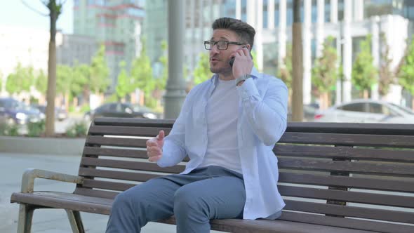 Man Talking on Phone While Sitting Outdoor on Bench