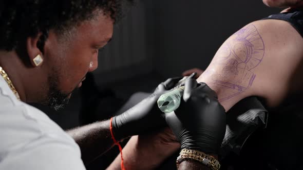 Professional African American Tattoo Artist Makes a Tattoo on Client Arm