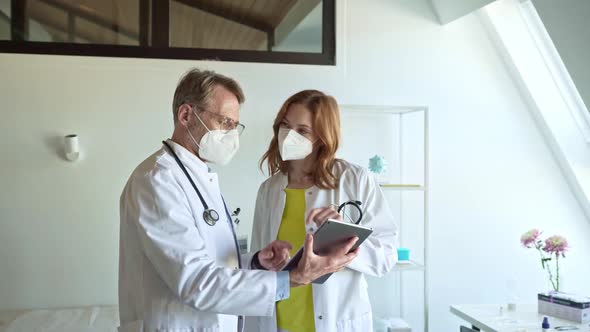 Doctor wearing face masks discussing over digital tablet in practice