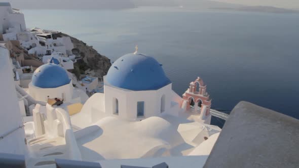Picturesque view of blue church domes and a pink church bell in Oia, Santorini.