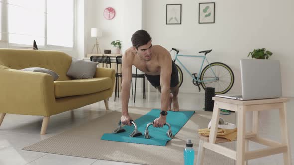 Young Fitness Man Doing Push Ups While Following a Tutorial Video on Laptop