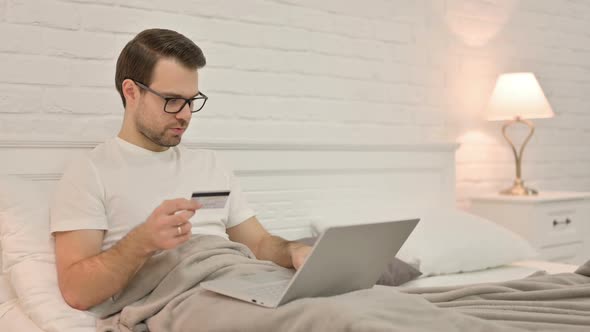 Young Man Online Shopping Success on Laptop in Bed