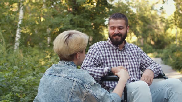 Happy Man is Sitting on Wheelchair and Talking to Woman Holding Hands