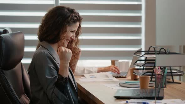 Caucasian business woman working at computer in office making victory gesture receives good news fro