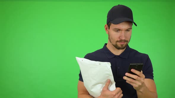 A Young Handsome Mailman Works on a Smartphone, Then Smiles at the Camera - Green Screen Studio