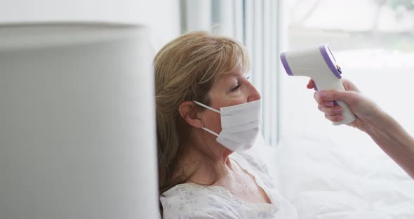 Senior woman wearing face mask getting her temperature measured at home