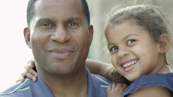 Father and daughter, in his arms, looking at the camera.