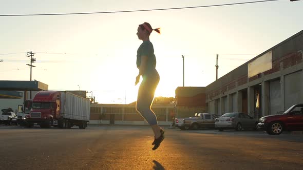 Silhouette of a young woman jump roping in the streets of an urban environment.