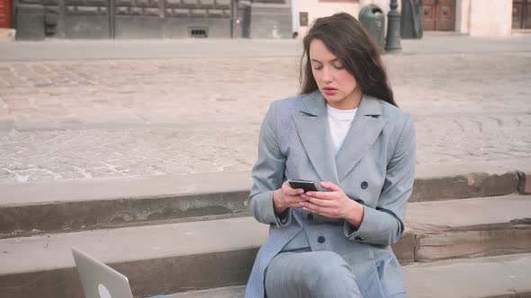 Young Woman Sitting on Stairs While Using Phone on the Street