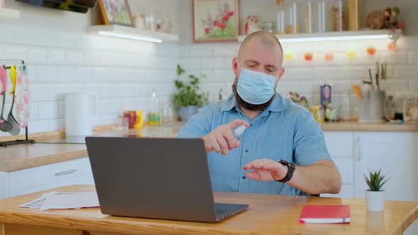 Senior Man Wearing Medical Protective Mask Uses Hand Sanitizer While Working or Studying Remotely at