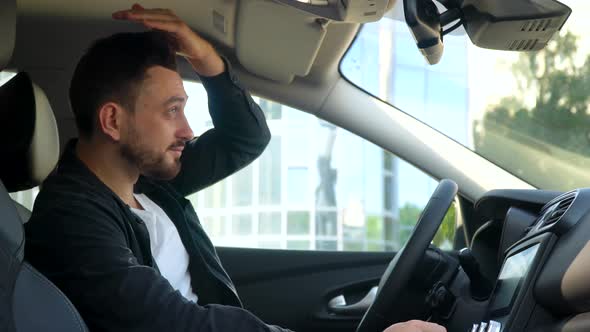 Bearded Man Looks in the Rearview Mirror in the Car Near Business Center